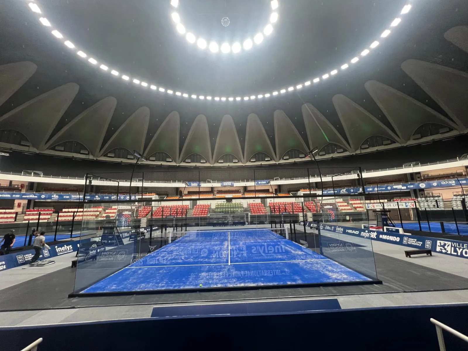 Pista de pádel azul en estadio moderno con techo curvo iluminado