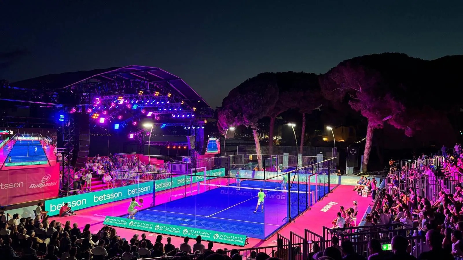 Vista elevada de pista de pádel azul en evento nocturno con espectadores