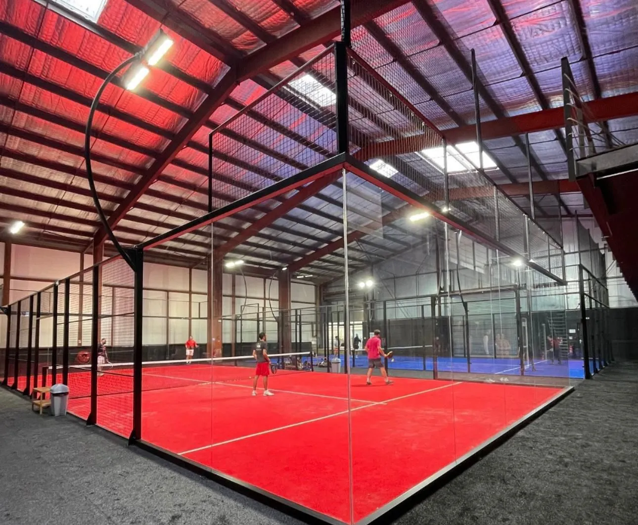 Pista de pádel individual con suelo rojo y jugadores en acción